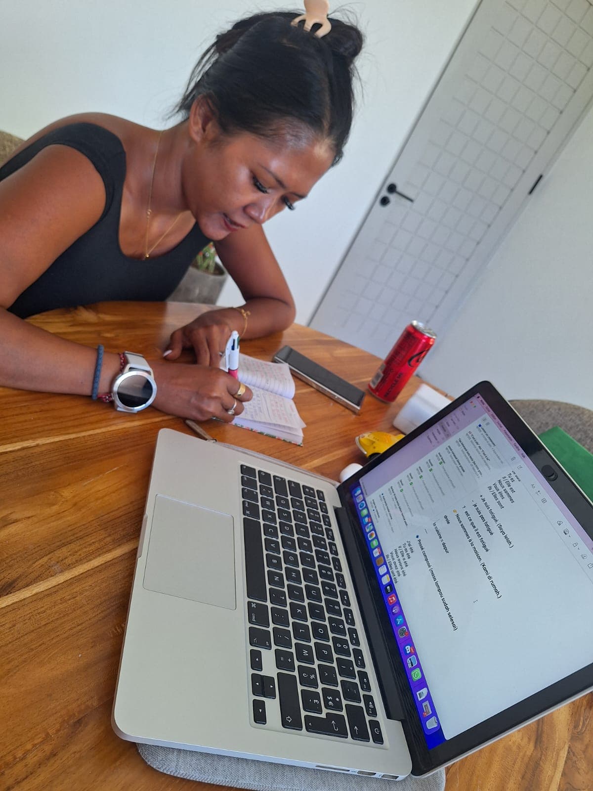 Femme prenant des notes dans un carnet devant son ordinateur portable sur une table.