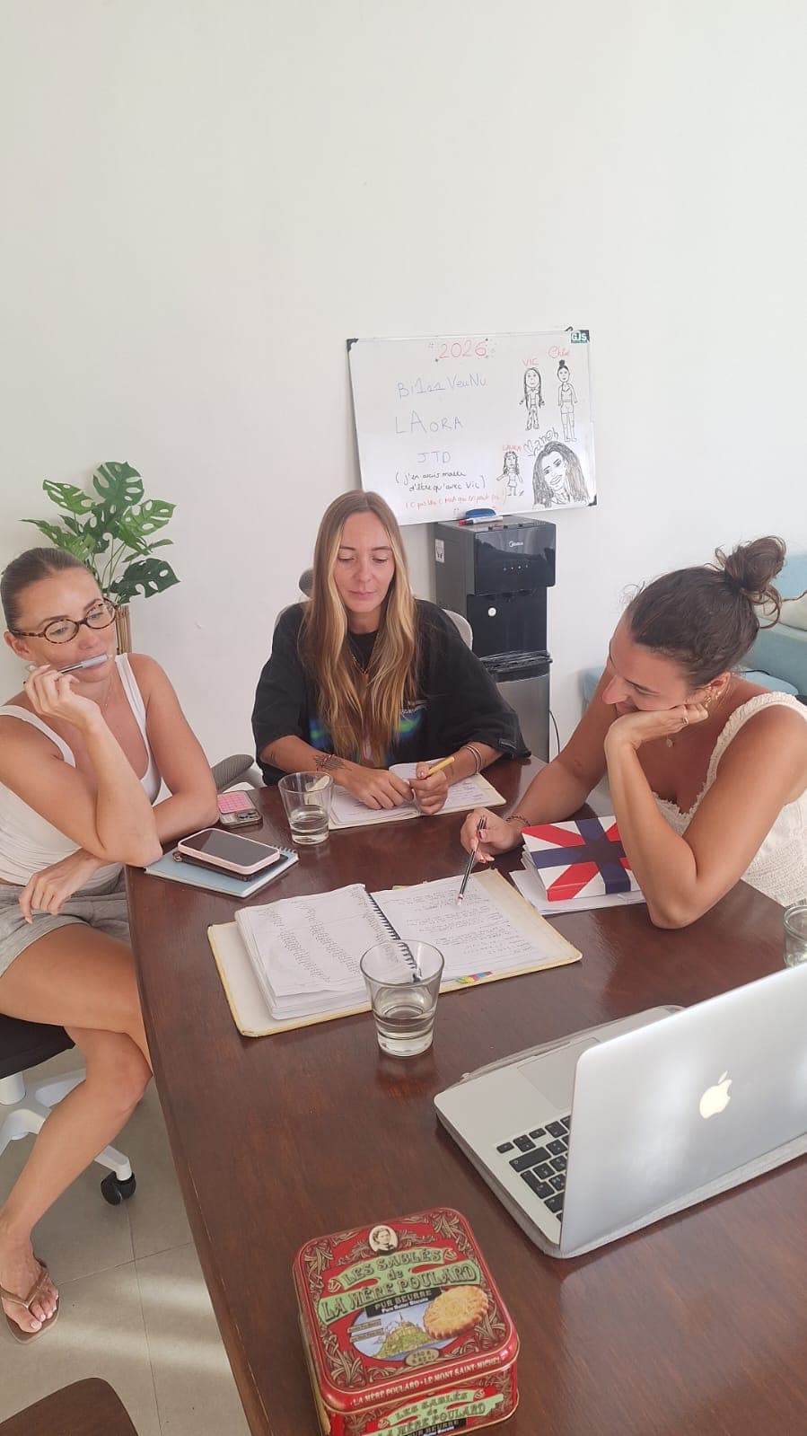 Trois femmes collaborent autour d'une table avec des cahiers et un ordinateur portable.