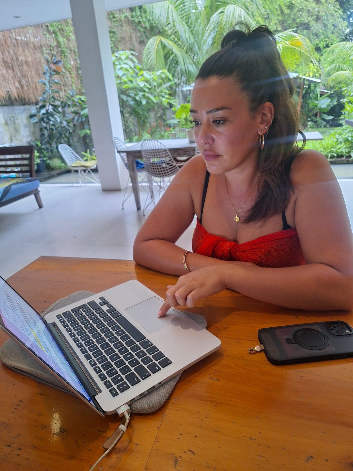 Femme utilisant son ordinateur portable sur une table en bois dans un patio tropical.