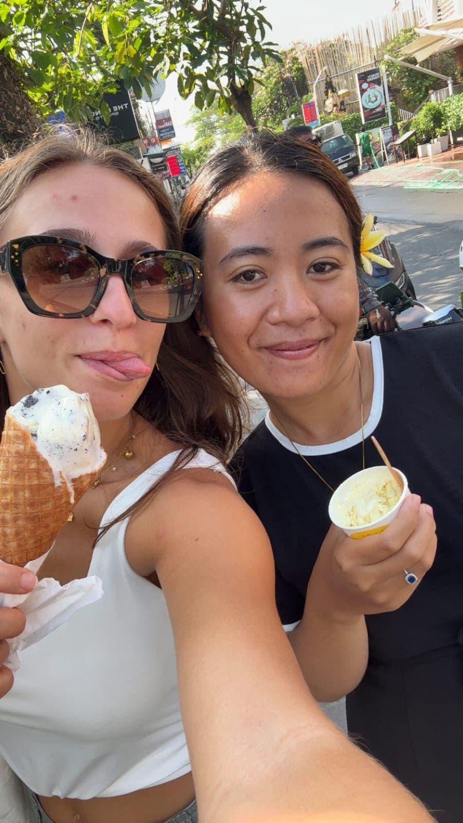 Deux femmes mangent des glaces dehors, l'une avec un cornet et l'autre un petit pot.