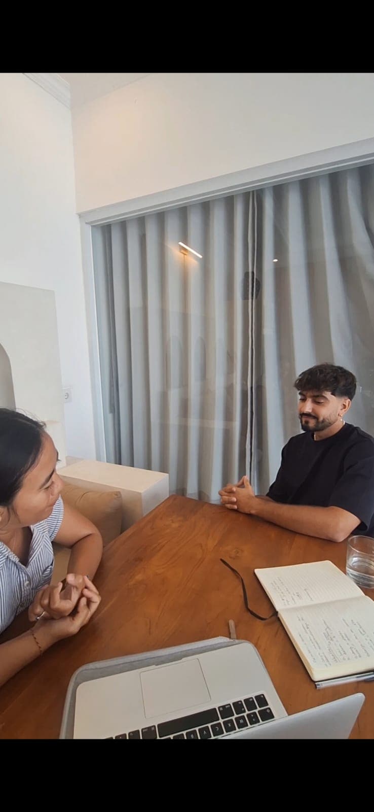 Homme et femme discutant à une table en bois avec un ordinateur et un carnet.