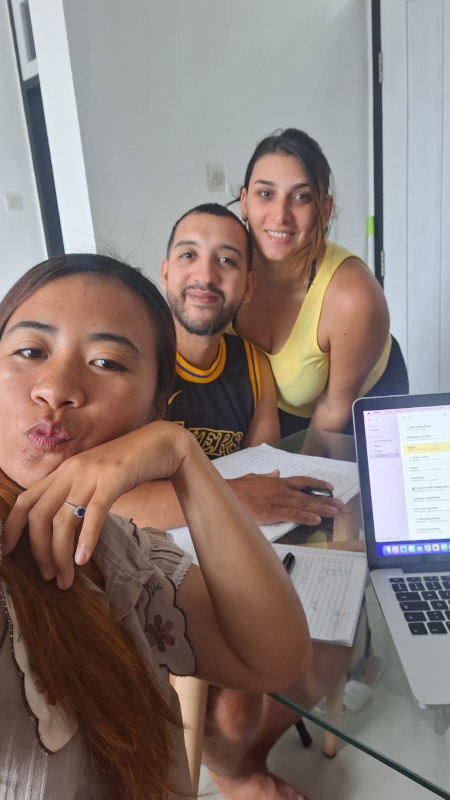Trois personnes posent pour un selfie devant un ordinateur portable et des notes manuscrites.