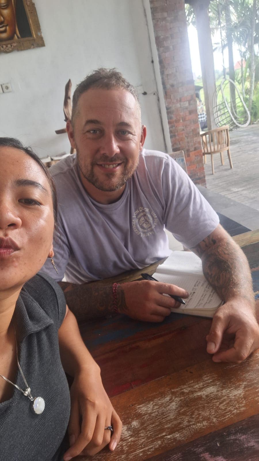 Homme tatoué souriant devant un carnet ouvert à côté d'une femme faisant une moue.